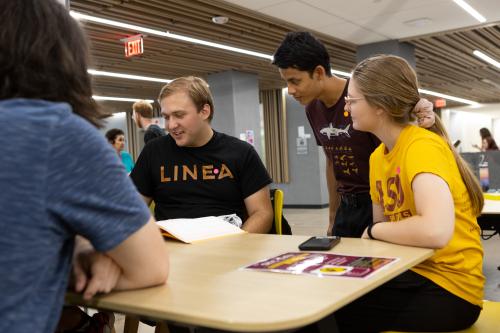 Students gathered around a table looking at a book of one of the students.